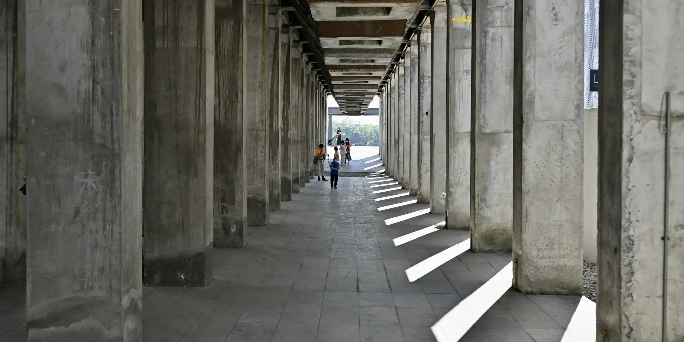People walking down a long concrete colonnade in morning light