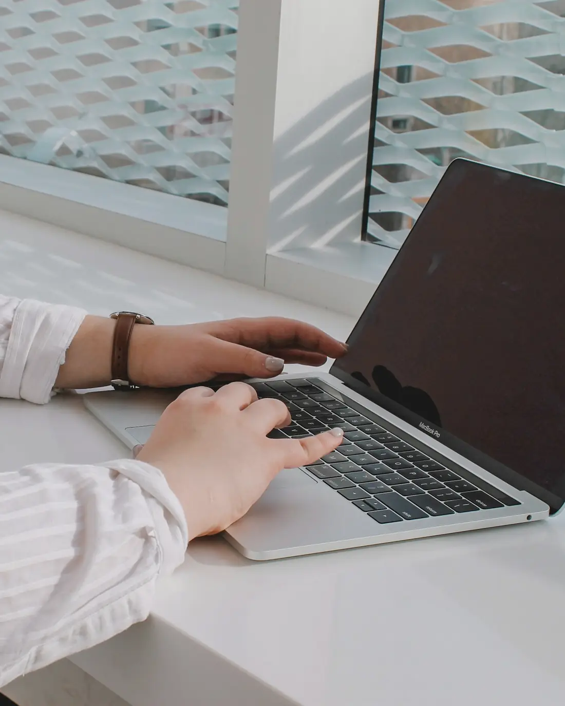 A person typing on a laptop at a bright white desk